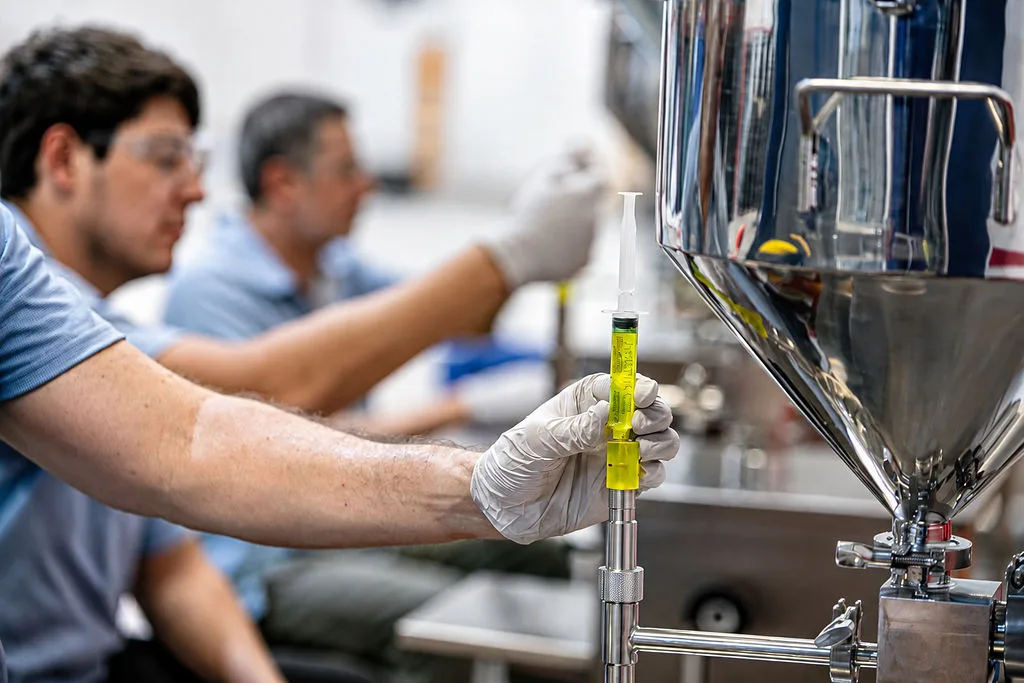 Proxima technician holding a syringe of fluorescent diagnostic fluid on the filling line